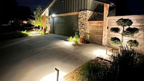 Una casa moderna con fachada de piedra, puerta de garaje de madera y un camino bien iluminado.