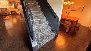 Una scala con tappeto decorato conduce a una sala da pranzo con un tavolo e sedie in legno.