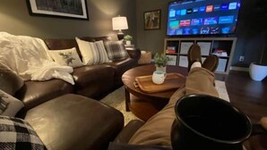 Un soggiorno con un divano in pelle marrone, un tavolino da caffè e un televisore che mostra diversi canali.