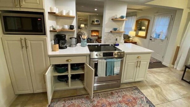Una cucina compatta con mobili bianchi, un forno a microonde integrato, un fornello e una macchina da caffè.