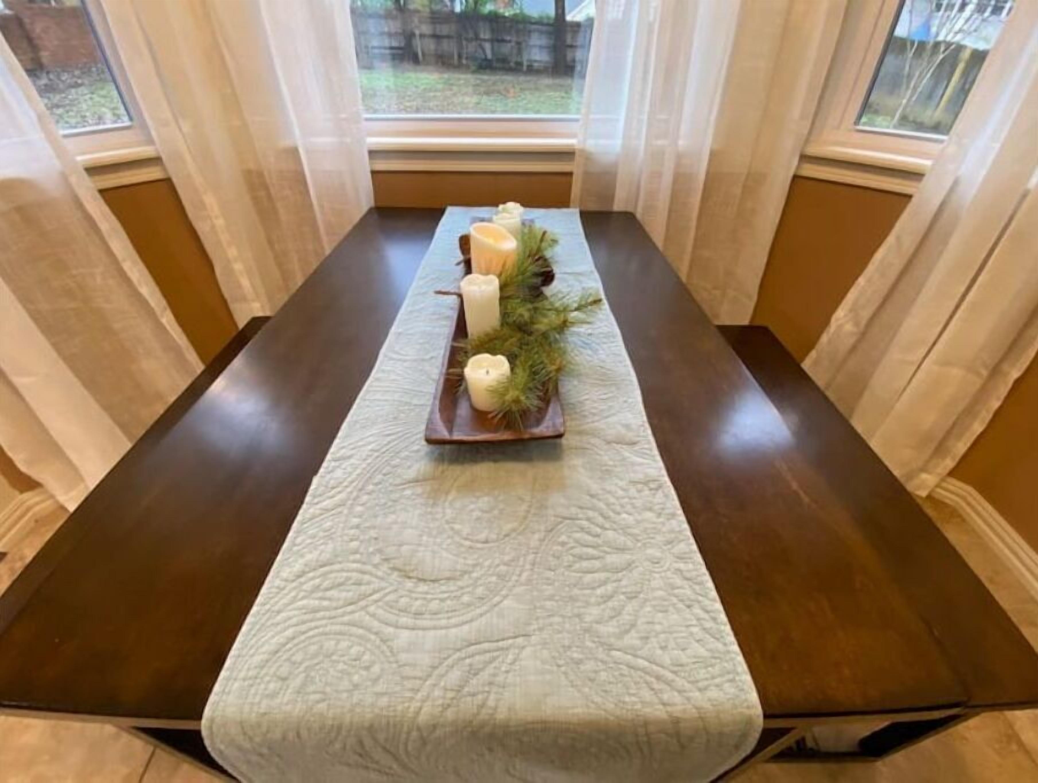 Una mesa de comedor con un camino de mesa blanco texturizado, velas y un pequeño centro de mesa con planta.