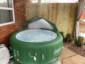 A green inflatable hot tub with a handle and a brand label, placed outdoors near a brick wall and a wooden fence. - "The Big Cozy"- WiFi, Hot tub, Grill, Sleeps 8 (Tulsa)