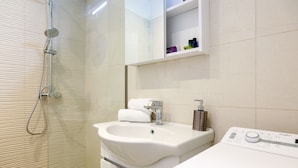 A modern bathroom with a glass shower enclosure, a white sink, and a built-in washing machine.