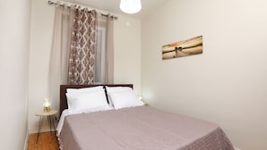 A bedroom with a bed, curtains, a bedside table with a lamp, and a painting on the wall.