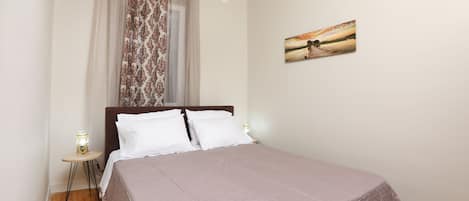Quarto com cama, cortinas, mesa de cabeceira com luminária e um quadro na parede.