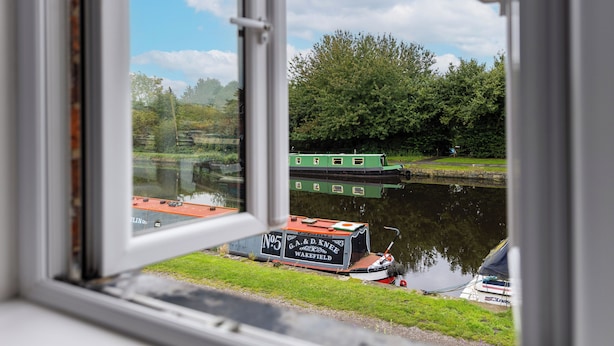 A view of a green boat docked at a canal, with a grassy bank and trees in the background. - 3 Bed 1.5 Bath | Canal Side Location | Close To Wakefield & Leeds | Pets Welcome (Stanley)