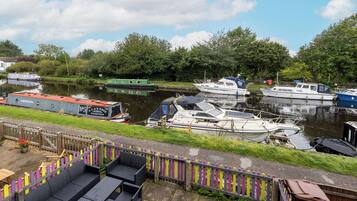 A riverside dock with various boats, a wooden fence, and outdoor seating.