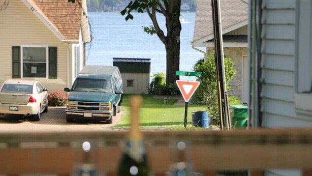 A residential street with parked cars, a yield sign, and a house with a view of a body of water. - Indian Lake Cottage for Nature Lovers - Apt A

 (Dowagiac)