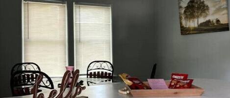 Une cuisine avec un plan de travail blanc, deux chaises, un panneau indiquant « Bonjour », un ventilateur de plafond et un tableau accroché au mur.
