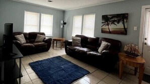 A spacious living room with two leather sofas, a blue rug, and a television on a stand. - Indian Lake Cottage for Nature Lovers - Apt A

 (Dowagiac)