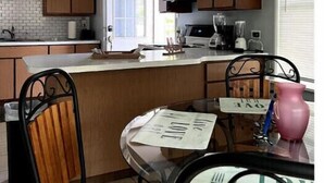 A modern kitchen with wooden cabinets, a central island, and a dining area with a table and chairs. - Indian Lake Cottage for Nature Lovers - Apt A

 (Dowagiac)
