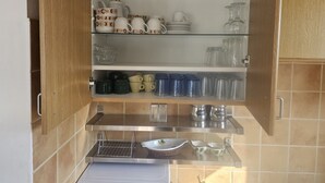 Ett kök med träskåp, en glashylla och diverse köksredskap, inklusive koppar, skålar och en kaffebryggare.