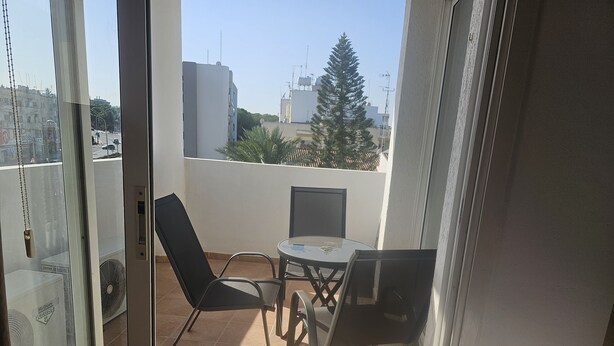 En balkong med ett bord och två stolar, en fläkt och utsikt över stadsbilden.