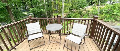 A wooden deck with two chairs and a table, surrounded by a wooden railing and lush greenery.