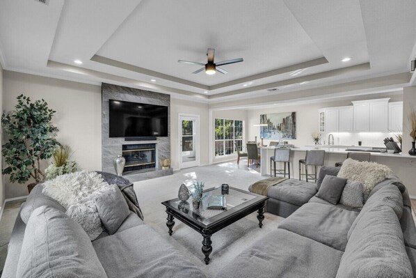A spacious living room with a large gray sofa, a glass coffee table, and a fireplace. - The Tulsacation on Oxford (Tulsa)