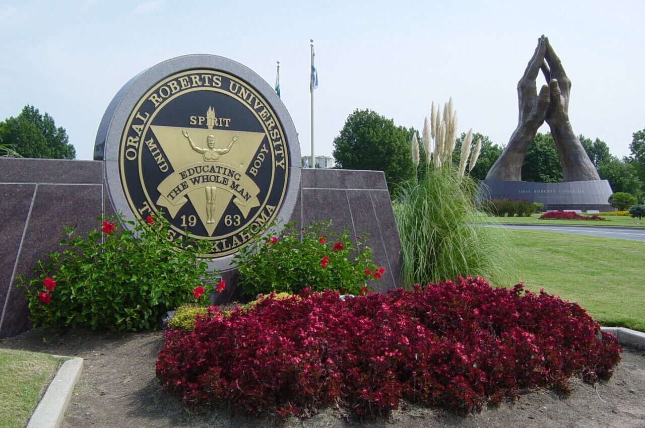 A university seal with a sculpture of hands above it.