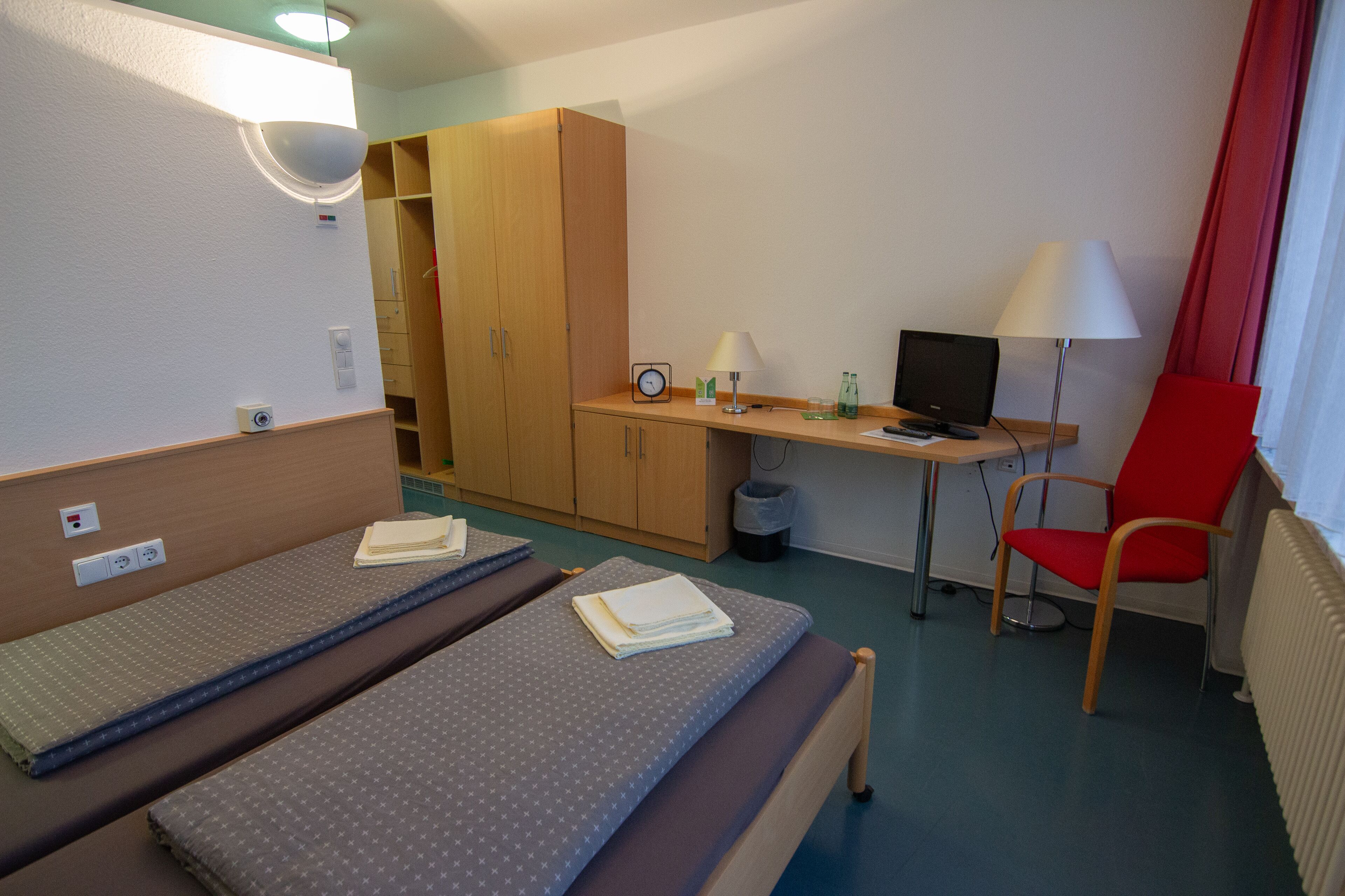 Habitación de hotel con dos camas, un escritorio con computadora, una silla y un armario.