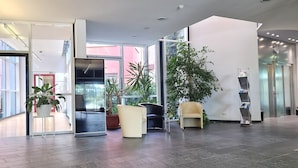 A spacious lobby with a modern design, featuring a large potted plant, seating area, and a reception desk. - Green Night Hotel (Falkenstein/Vogtl.)