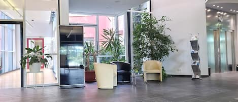 Un vestíbulo amplio con diseño moderno, que incluye una gran planta en maceta, una zona de estar y una recepción.
