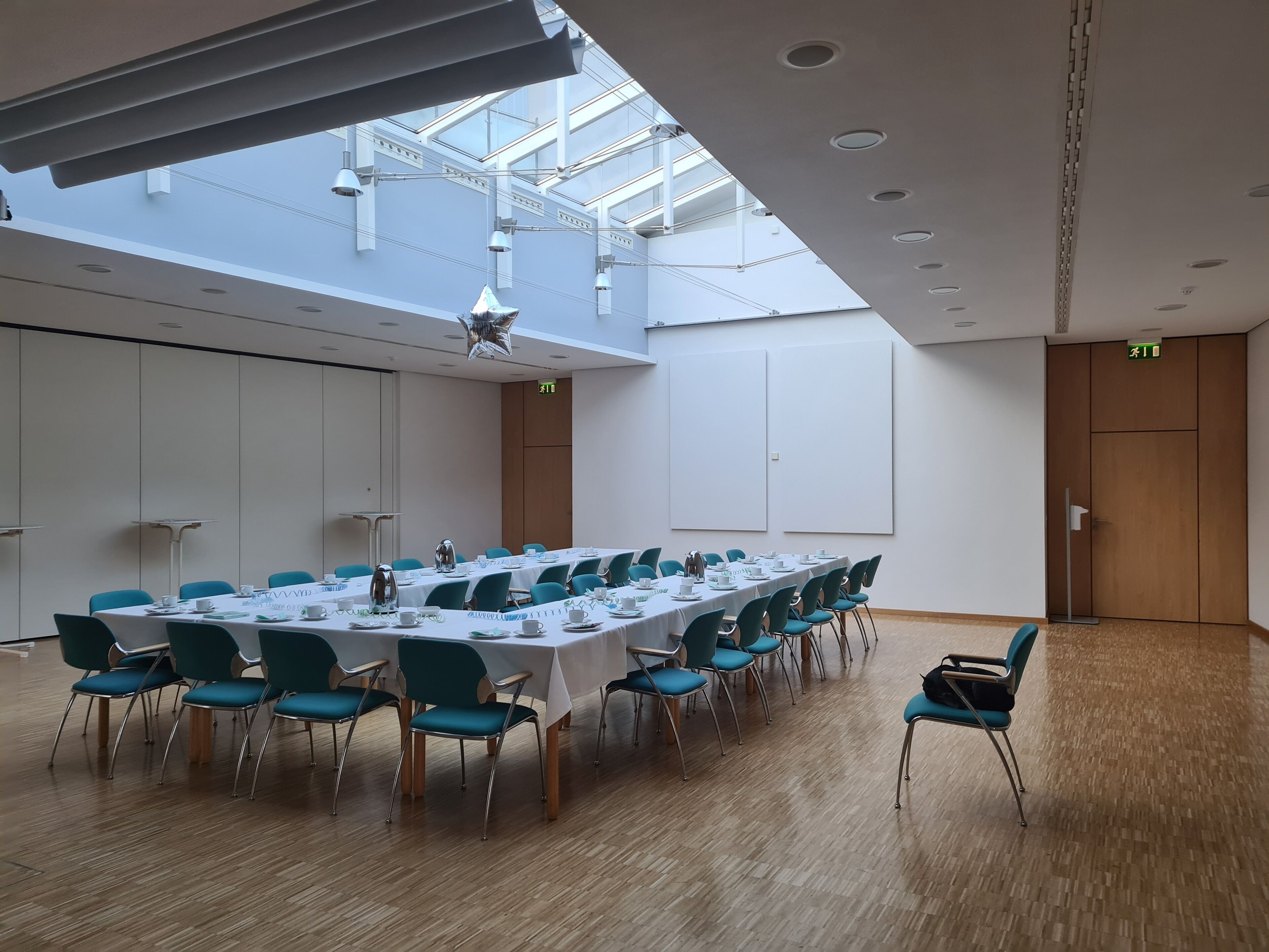 A conference room with a long table, teal chairs, and a high ceiling with skylights.