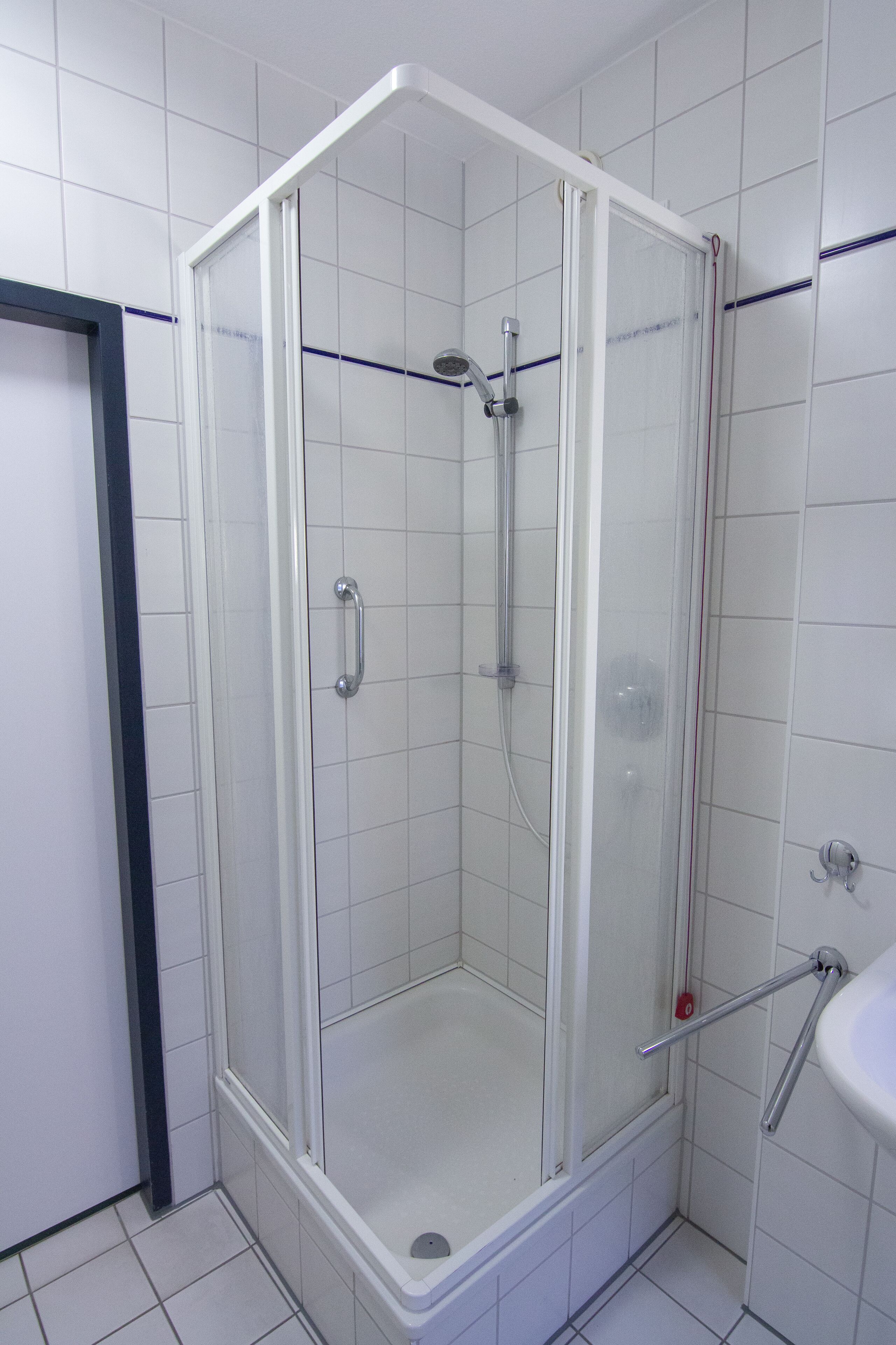 Cabina de ducha con paredes de vidrio, regadera de mano y llave de agua de mano.