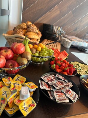 A breakfast buffet with various fruits, bread, and packaged snacks.