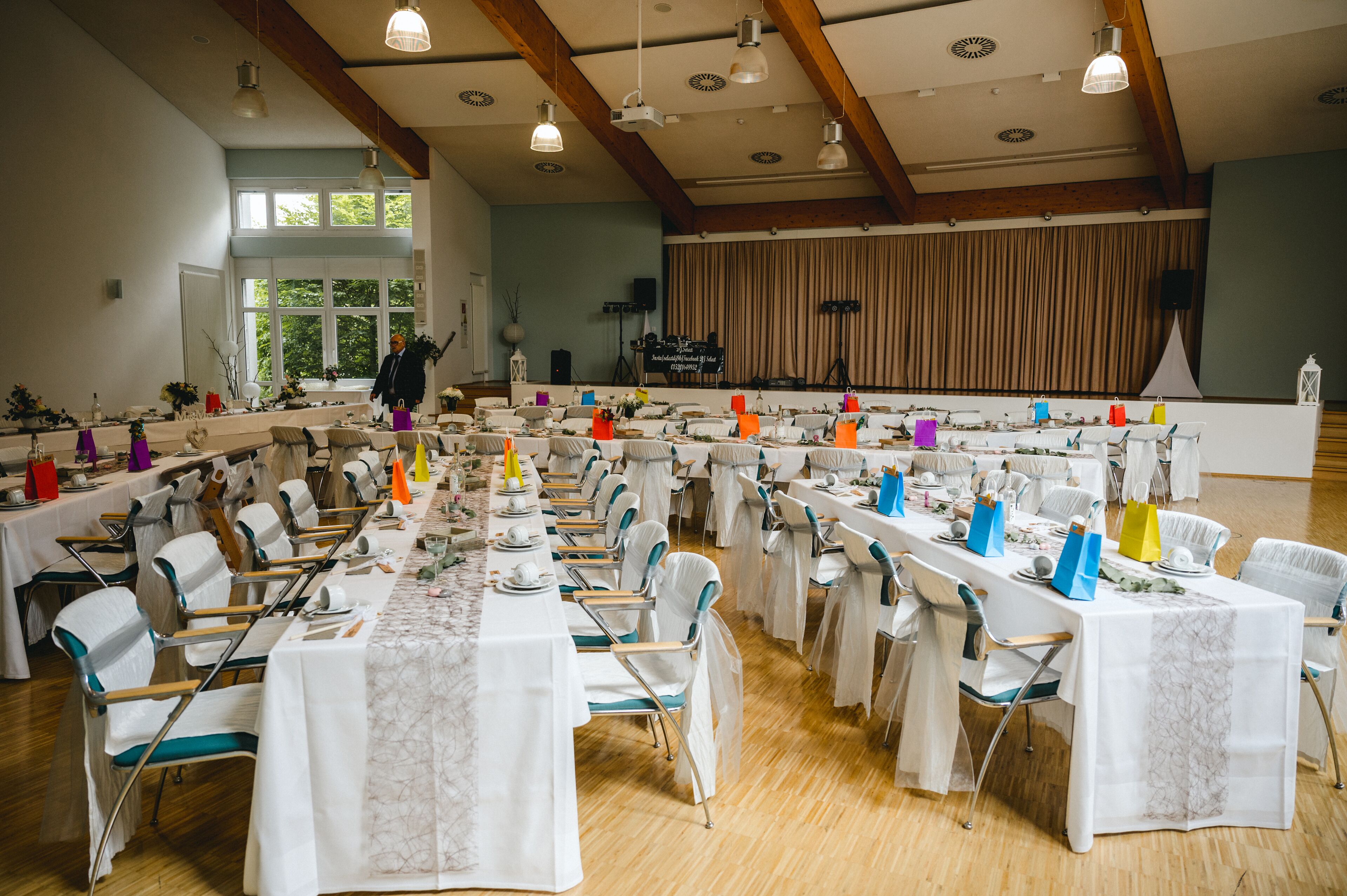 En festlokal med långa bord uppdukade för ett formellt evenemang, träbjälkar i taket och en scen med draperier i bakgrunden.
