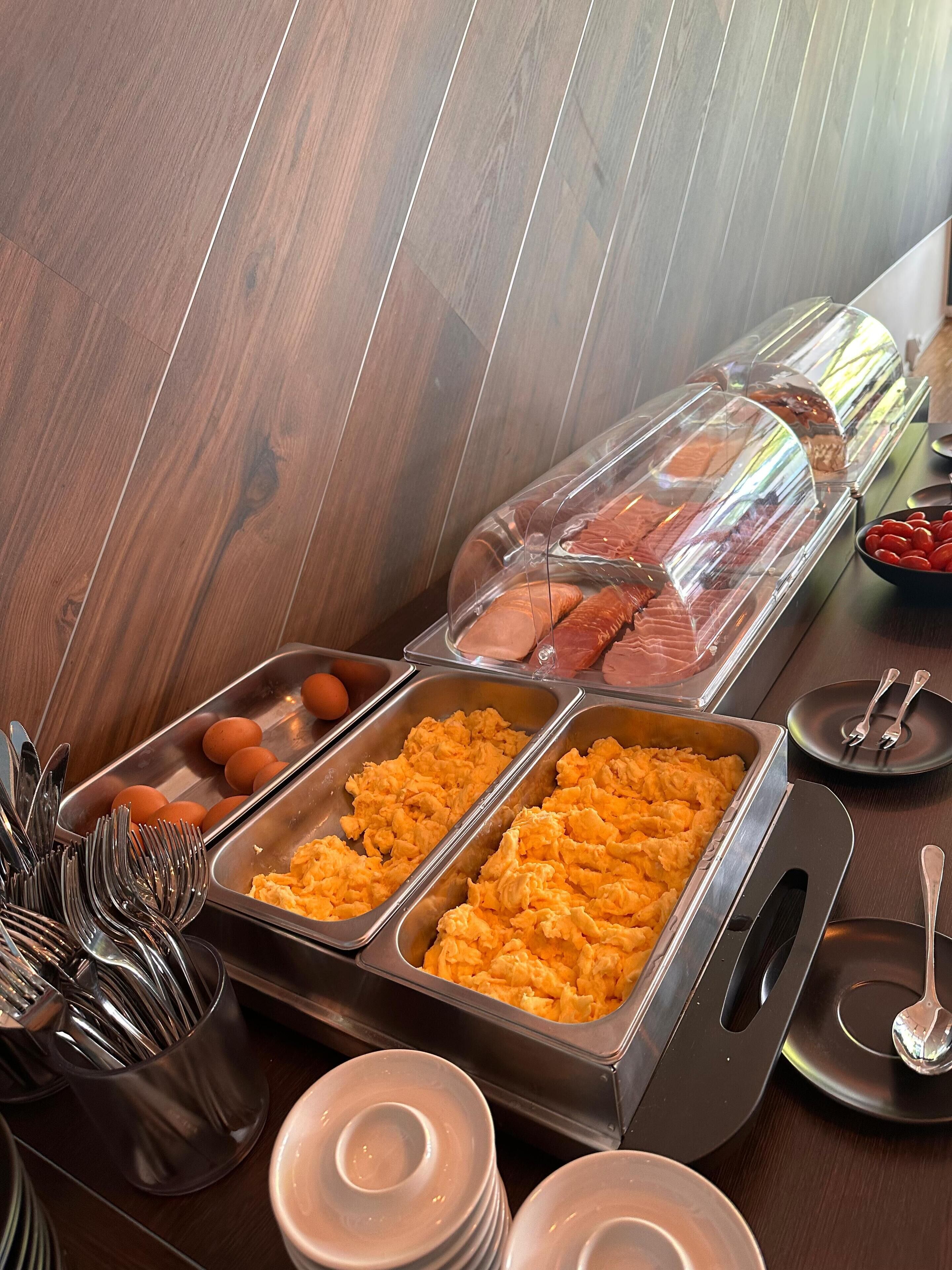 A buffet setup with scrambled eggs, sausages, and eggs in separate trays.