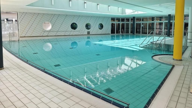 An indoor swimming pool with clear water, tiled walls, and a yellow pillar. - Green Night Hotel (Falkenstein/Vogtl.)