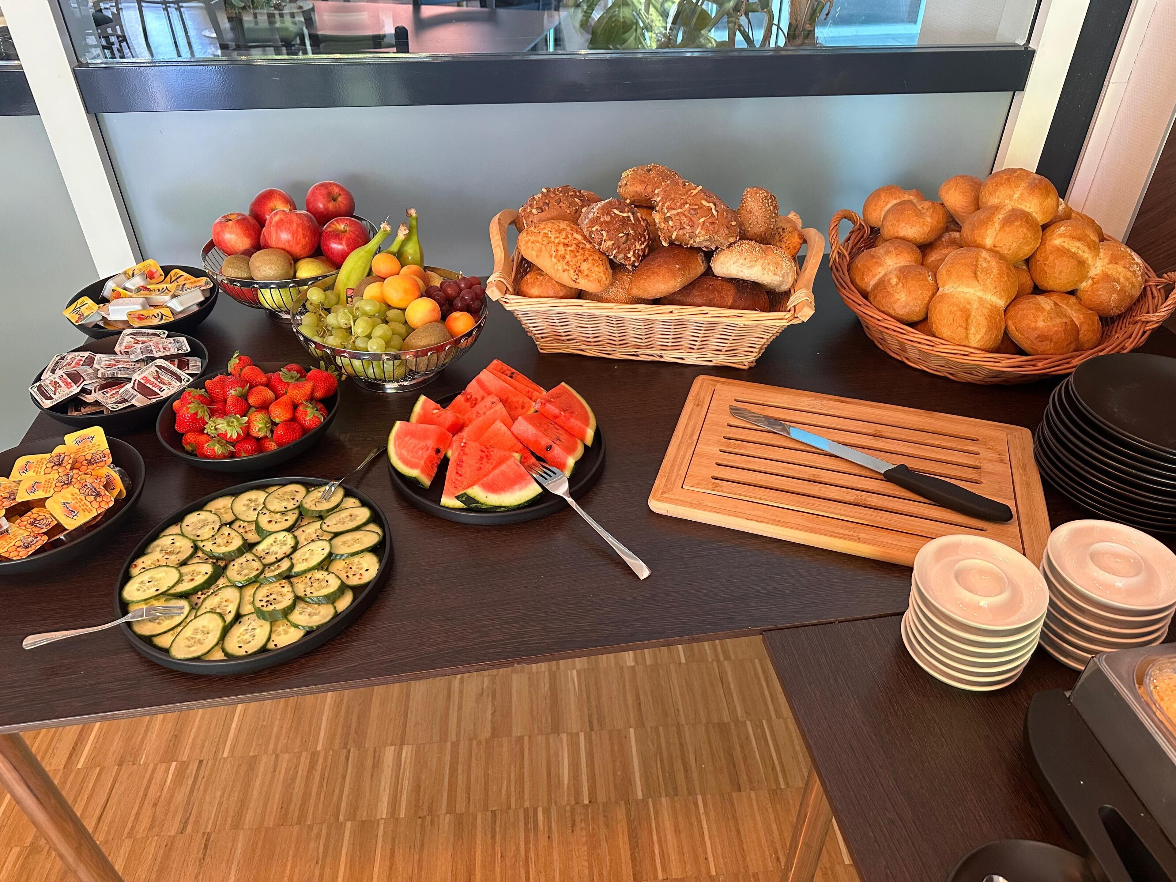 A buffet table with various food items including fruits, bread, and sliced vegetables.