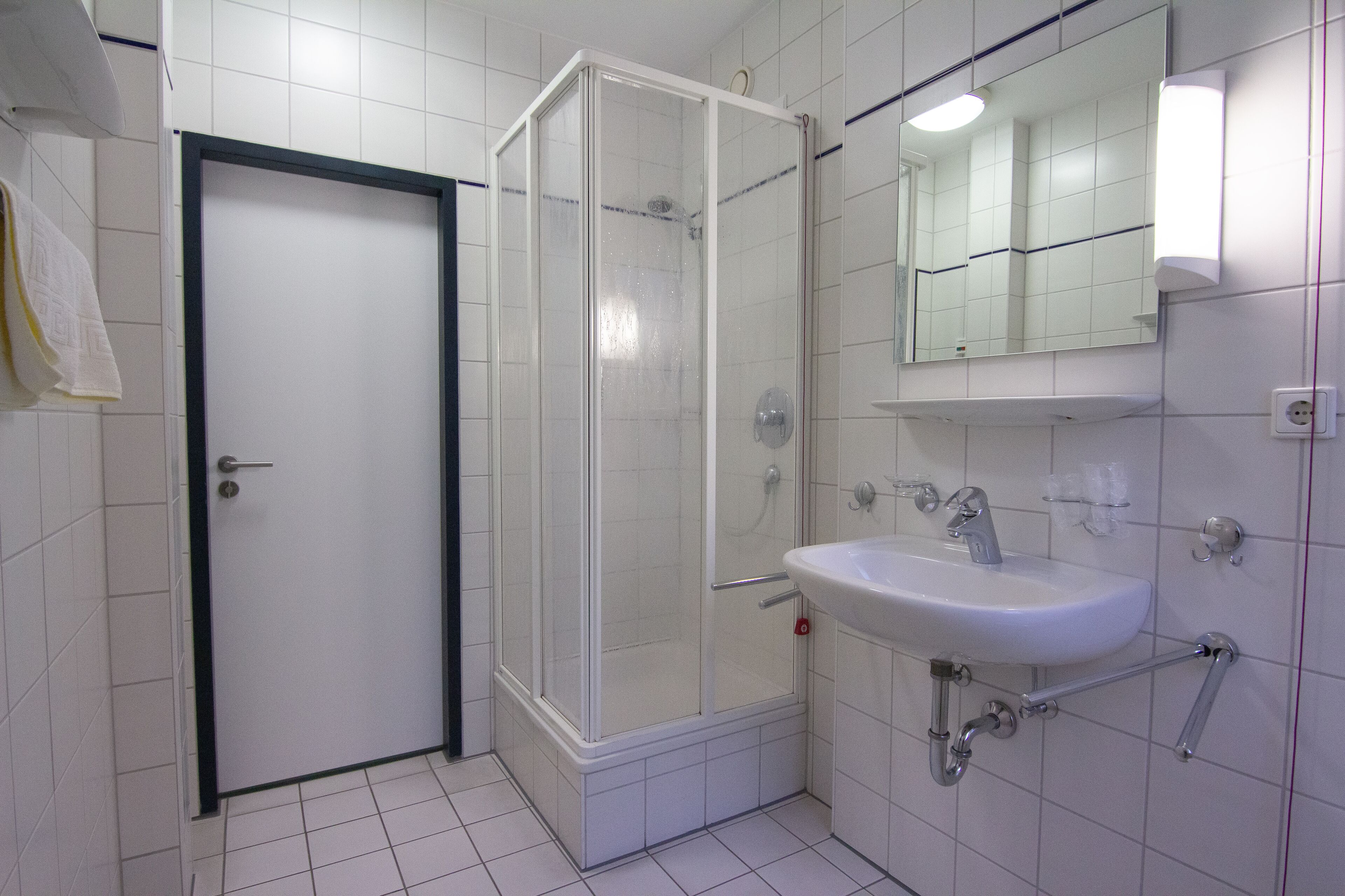 Un baño con lavamanos blanco, ducha con mampara de vidrio y una puerta.
