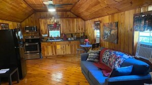 A cabin interior with a wooden interior, a kitchenette, a dining area, and a sofa. - Charming Cabin near Kentucky LK (Camden)