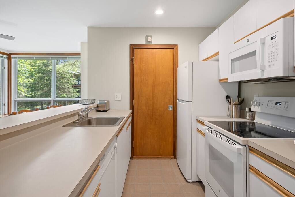 A modern kitchen with a wooden door, white cabinets, a built-in oven, and a microwave.