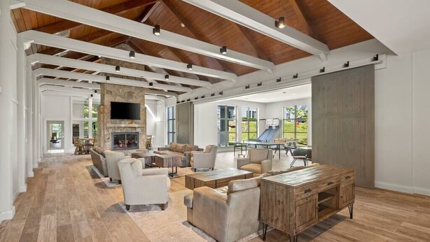 A spacious living room with a high ceiling, wooden beams, a fireplace, and a large window overlooking a backyard. - The Trailside Retreat | Ski on&off w/ Fireplace! (Dover)