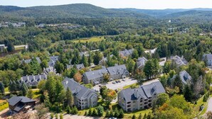 A residential area with multiple houses, surrounded by dense forest and hills in the background. - The Trailside Retreat | Ski on&off w/ Fireplace! (Dover)