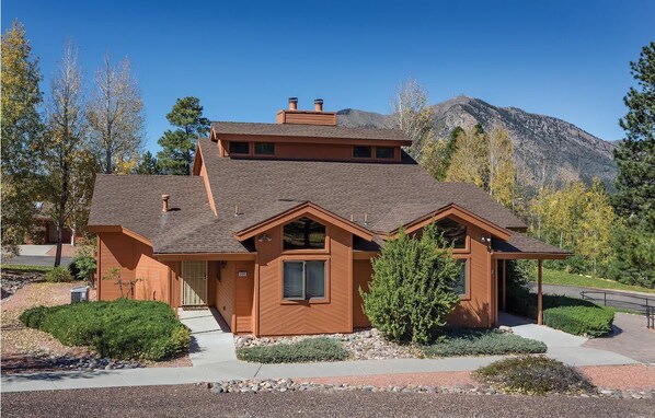 A modern two-story house with a sloped roof, a chimney, and a well-maintained front yard with landscaping. - 2Bed/2Bath Deluxe Suite in Flagstaff! Complete w/Golf, Pools, and More! (Flagstaff)