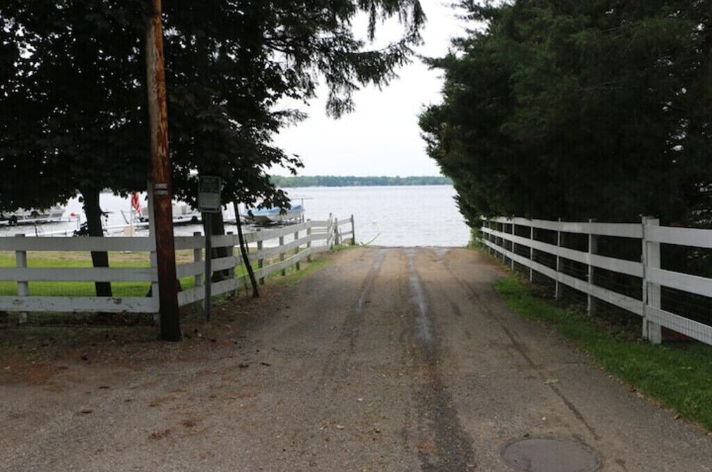A gravel path leading to a body of water, flanked by white fences and trees.