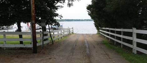 A gravel path leading to a body of water, flanked by white fences and trees.