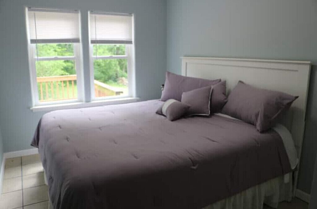 A bedroom with a bed, two windows, and a view of greenery outside.