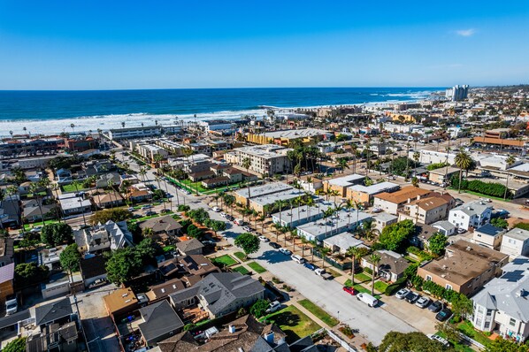 An aerial view of a coastal residential area with a mix of single-family homes and apartment buildings, a beach, and a pier in the background.