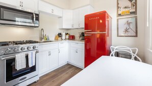 A modern kitchen with white cabinets, a red refrigerator, a stove, and a microwave.