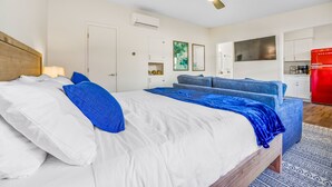 A modern bedroom with a large bed, a ceiling fan, a kitchenette, and a dining area.
