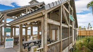 Une structure en bois située au bord de la plage, dotée d’un espace de repos couvert et d’une enseigne indiquant « Emerald Shores ».