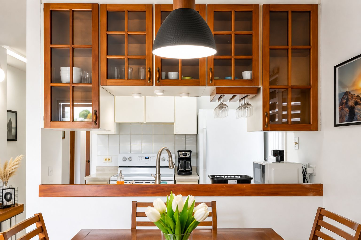 A kitchen with wooden cabinets, a central island, a dining table with chairs, and a pendant light.