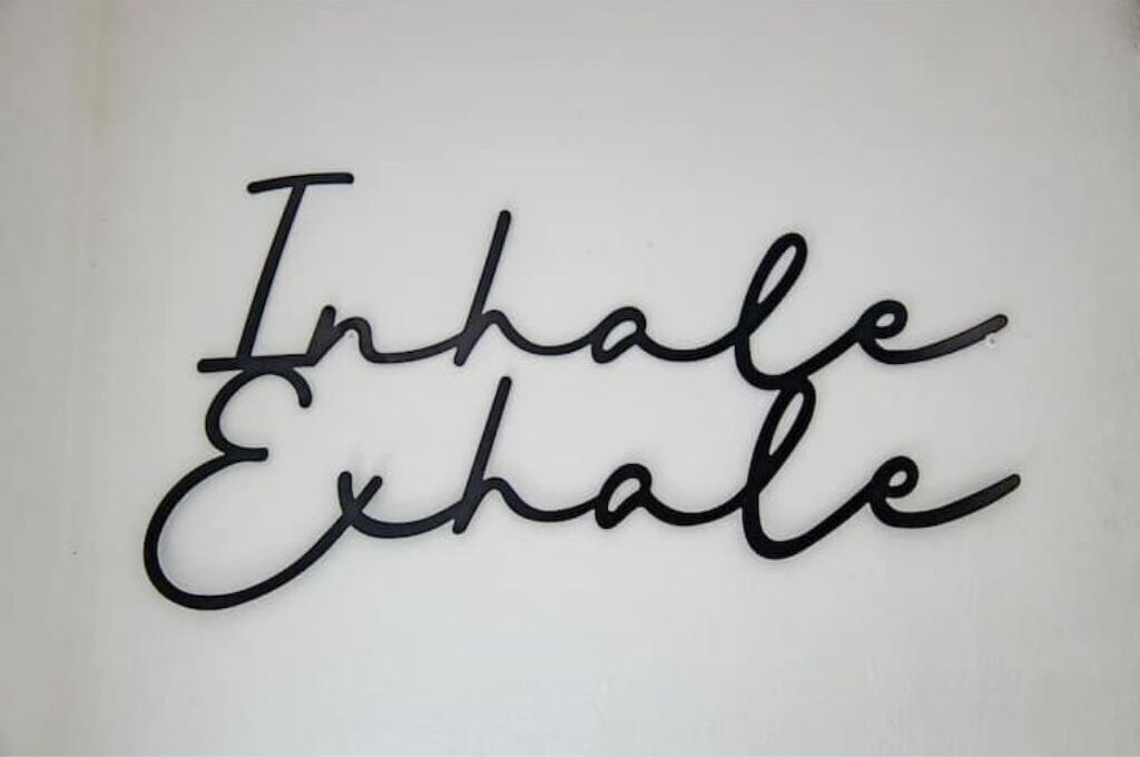 A wall with a black metal sign that reads "Inhale Exhale".