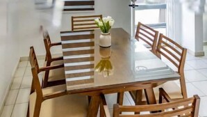 A dining area with a wooden table and chairs, a potted plant, and pendant lighting.