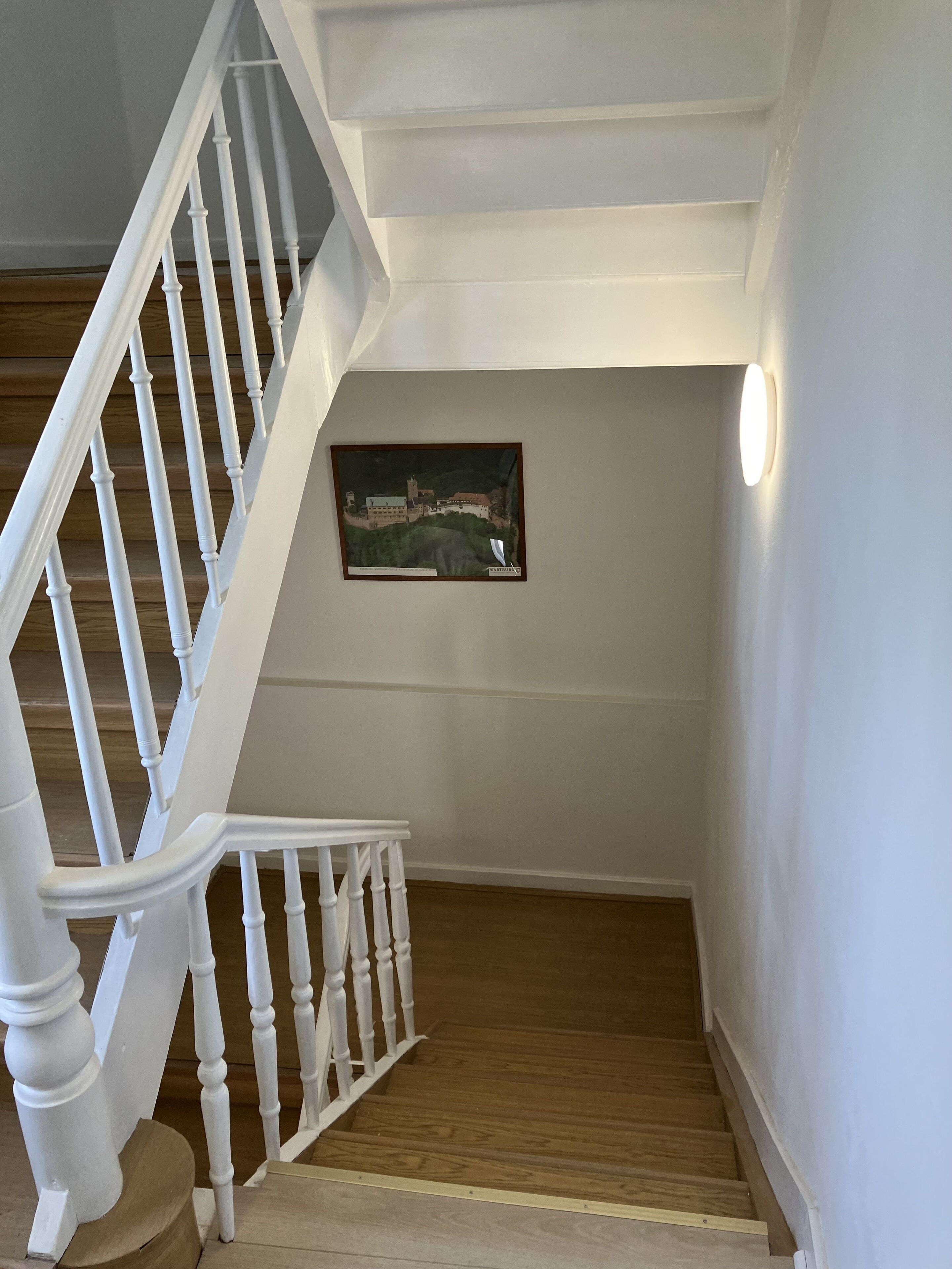 A staircase with white balusters leading to a landing with a framed picture on the wall.