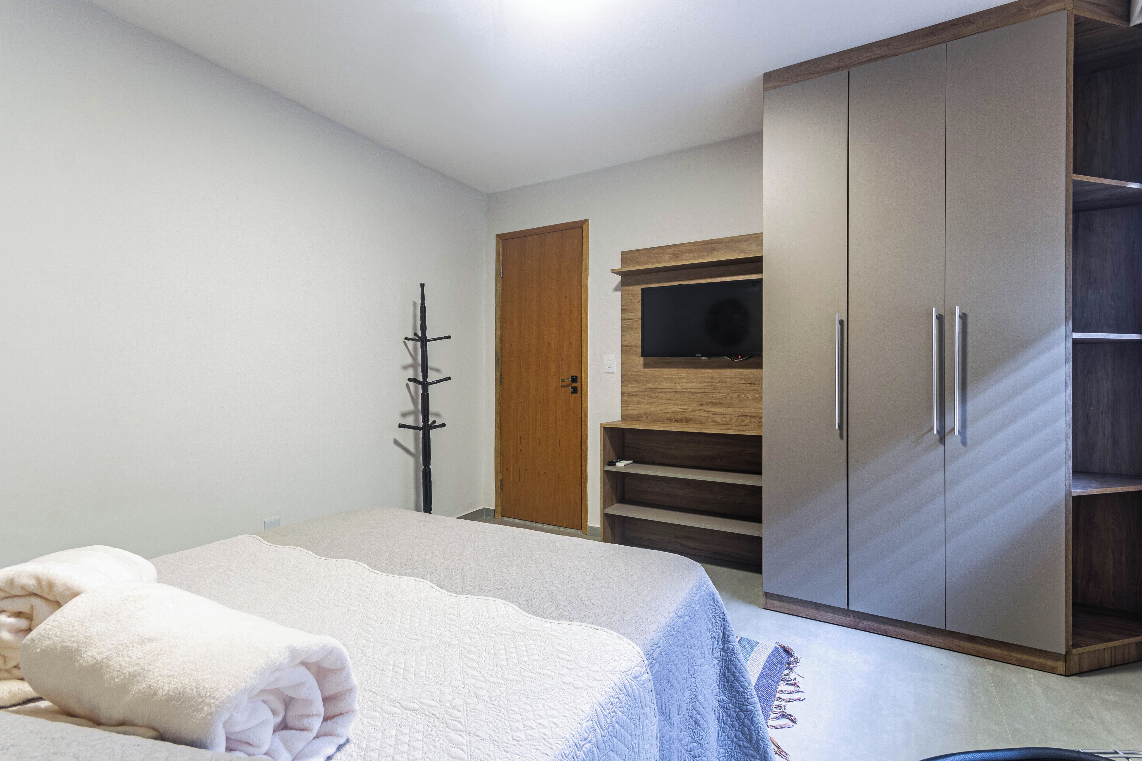 Un dormitorio con cama, armario, televisor y perchero.