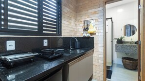 Een keuken met een zwart aanrecht, een spoelbak en een raam met jaloezieën.