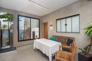 Una habitación con una mesa, sillas, un banco de madera, una planta en maceta y un ventanal con vistas.